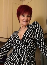 Mature redhead with short hair showing assets in the kitchen
