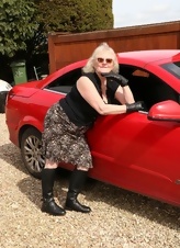 In these porn photos, a naked old lady with glasses poses next to a red car and caresses her body